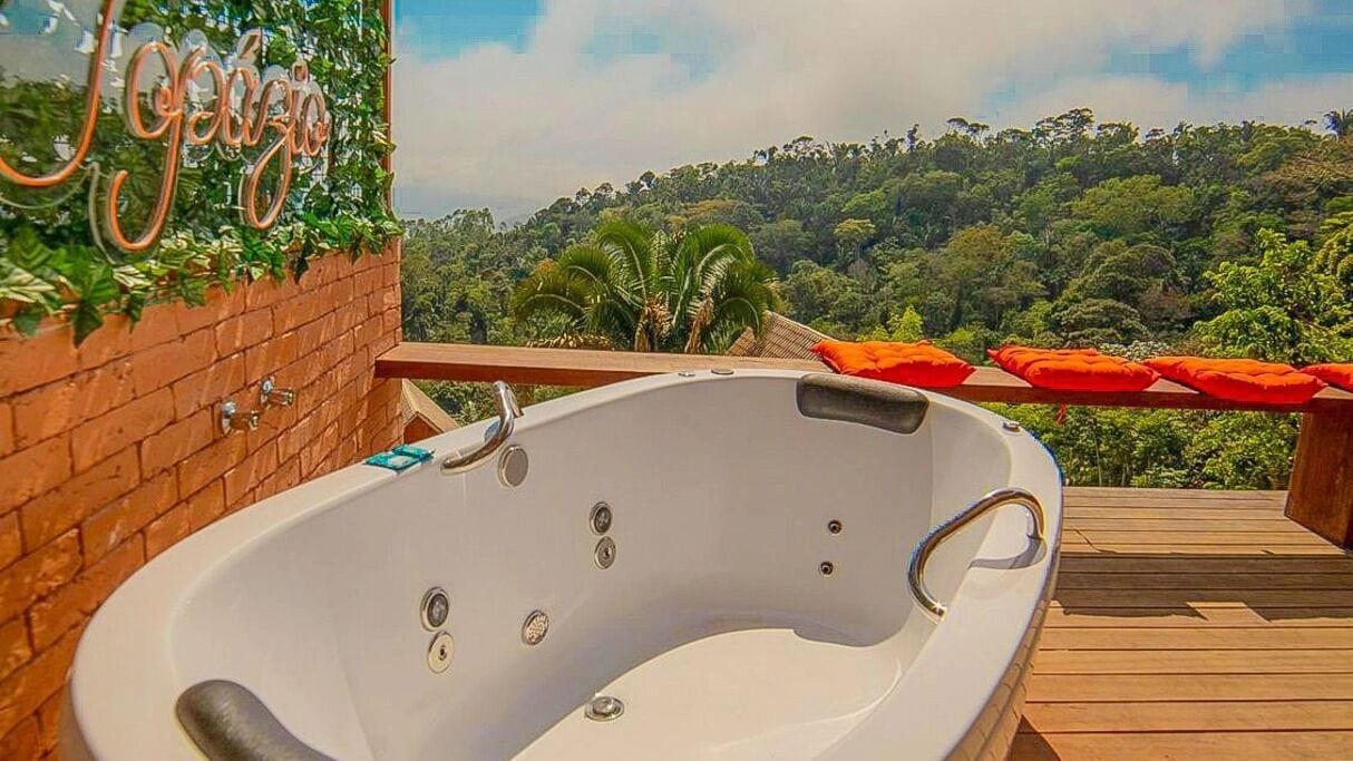 Uma banheira de hidromassagem em um deck de madeira com vista para uma floresta exuberante.