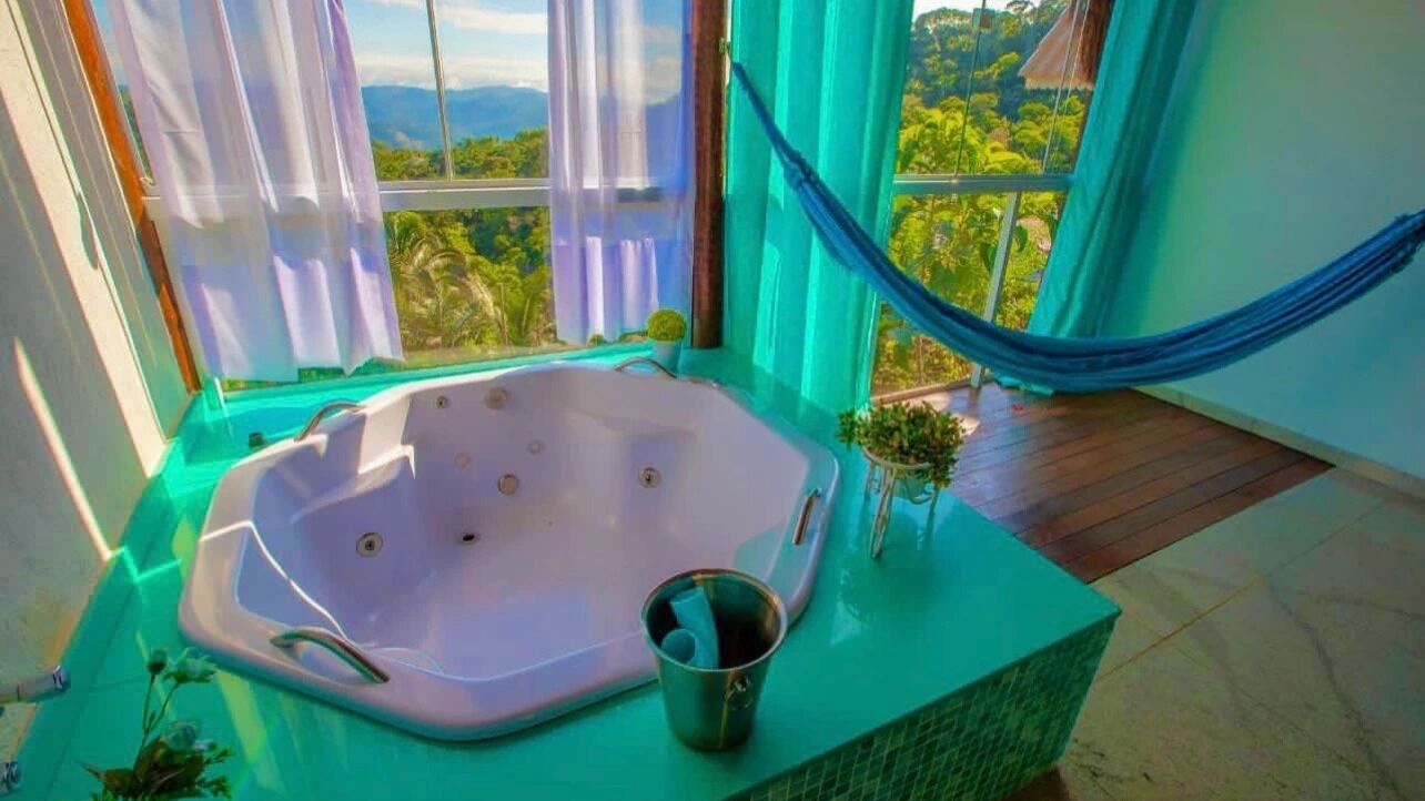 A room with a large bathtub, a hammock, and a view of a lush landscape.