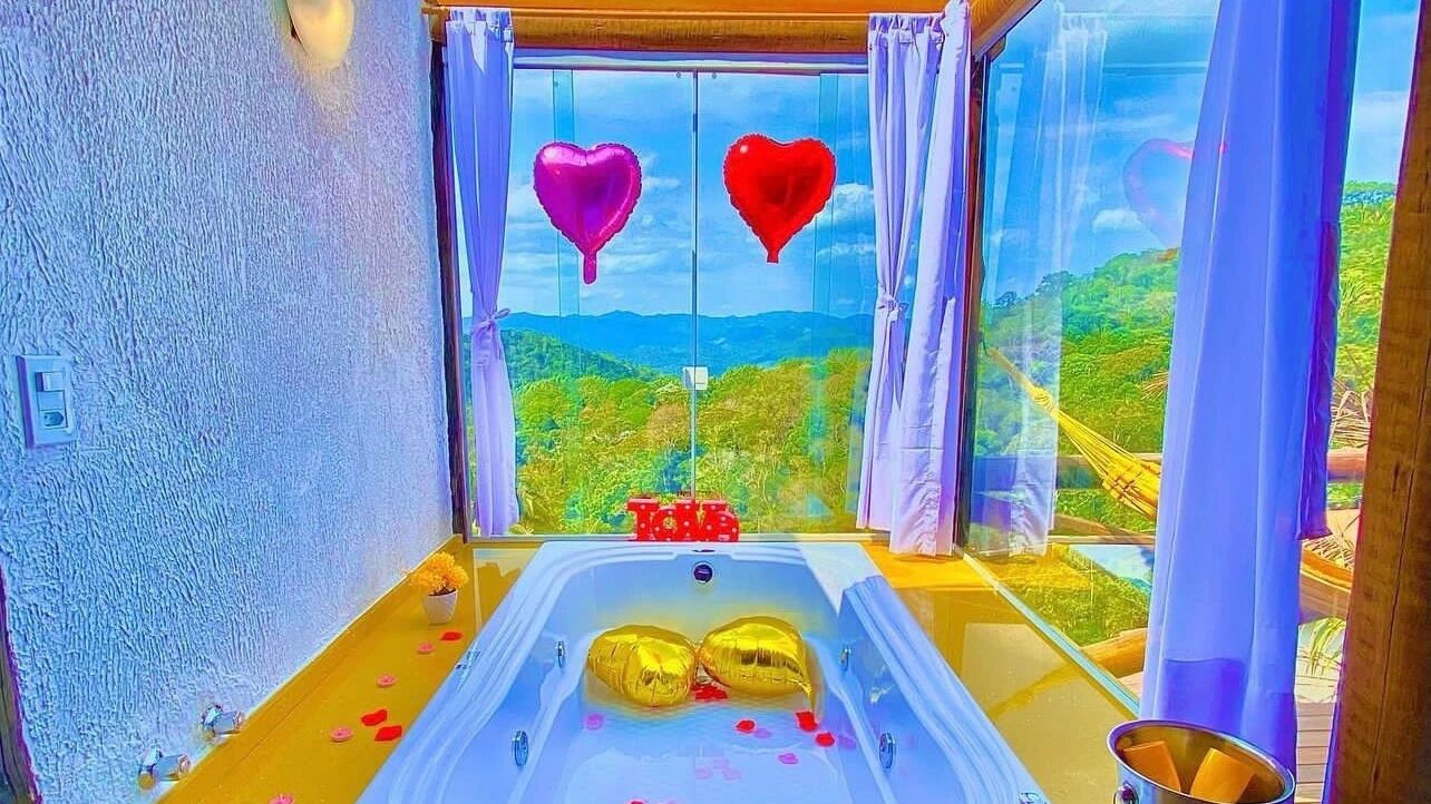 A room with a bathtub, a window with curtains, and a view of a landscape.