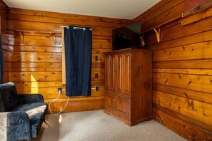 Une pièce aux murs en bois, avec un rideau bleu foncé, une armoire en bois et une chaise.