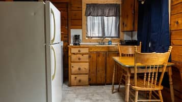 Une cuisine de taille réduite comprenant un réfrigérateur, des placards en bois, un évier et une chaise.