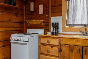 Une cuisine avec un four blanc, des placards en bois, une machine à café et une fenêtre avec un rideau.