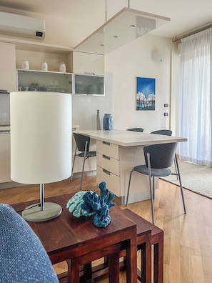 Cozinha moderna com armários brancos, sala de jantar com mesa e cadeiras, e uma grande janela com cortinas.