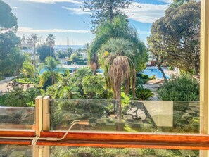 A view from a balcony overlooking a pool area with palm trees and a clear sky. - Mediterranee (Sanremo)