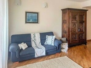 Un salon avec un canapé bleu, un meuble en bois et un tableau encadré accroché au mur.