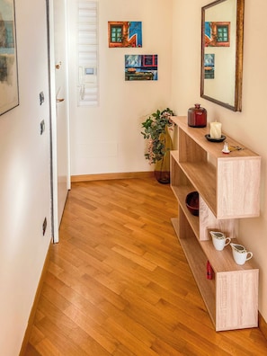 Corredor com piso de madeira, porta branca e um console de madeira decorado com objetos.