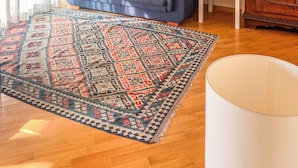 Una sala de estar con un sofá azul, un tapete estampado, un aparador de madera y una lámpara blanca.