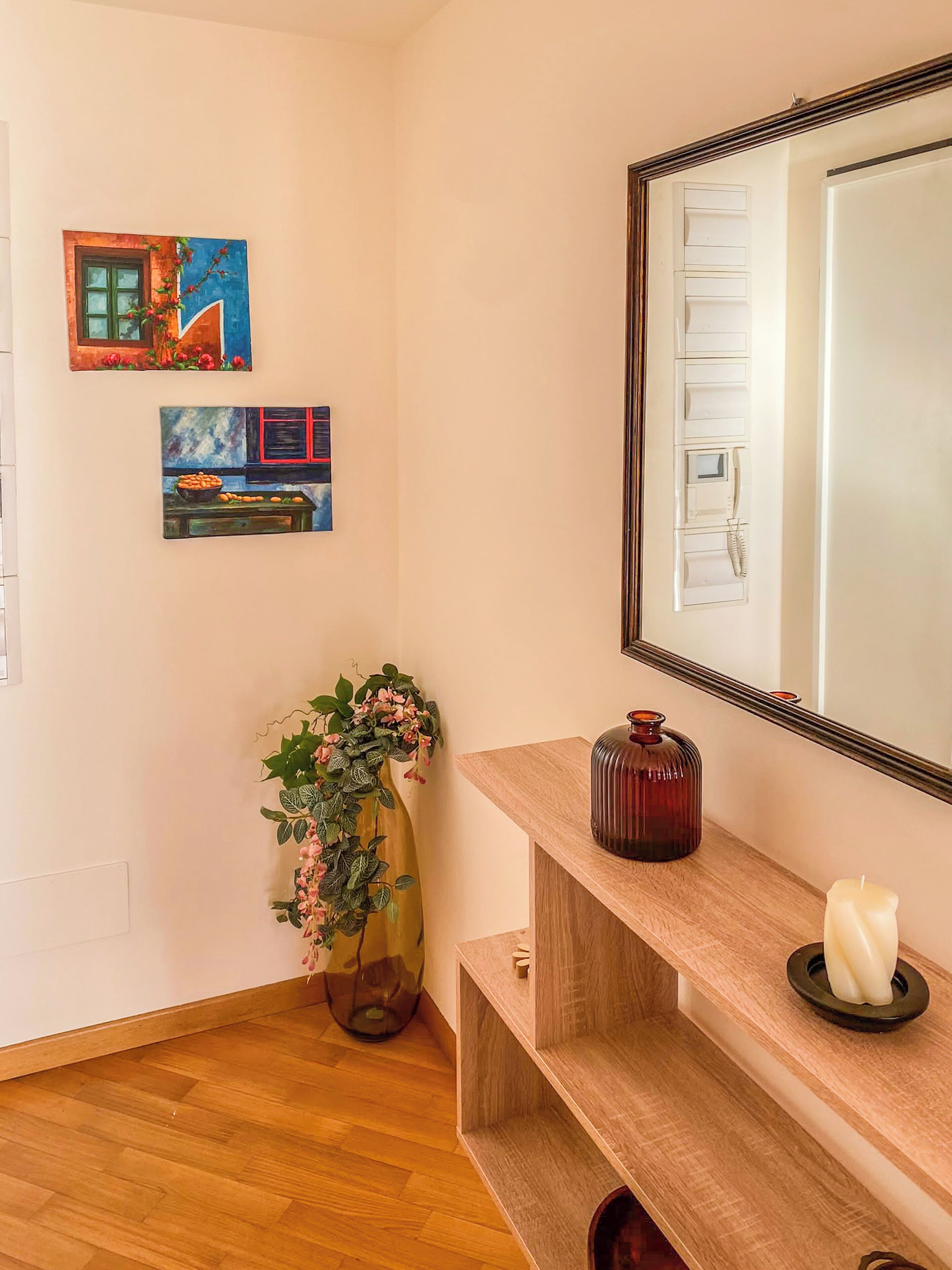 Un couloir avec un plancher en bois, un miroir, un vase de fleurs et deux tableaux accrochés au mur.
