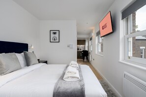 A hotel room with a bed, a TV, a framed picture, and a view of the kitchen. - GuestReady - Studio by the Maritime Museum (London)