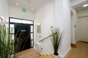 A hallway with a black door, a green exit sign, a framed picture, and a potted plant. - GuestReady - Studio by the Maritime Museum (London)