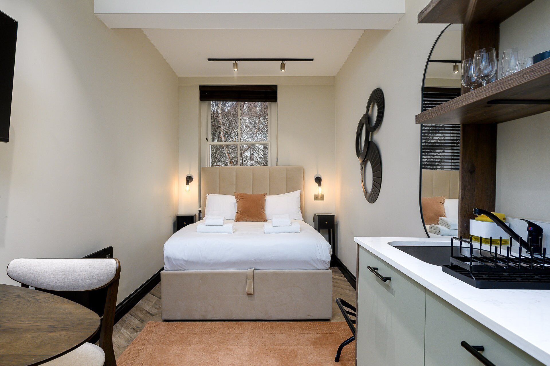 A modern bedroom with a bed, bedside tables, a chair, and a kitchenette.