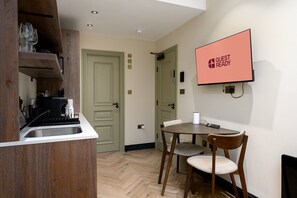 Eine kompakte Küche mit Spüle, einem Esstisch mit Stühlen und einem an der Wand befestigten Flachbildfernseher.