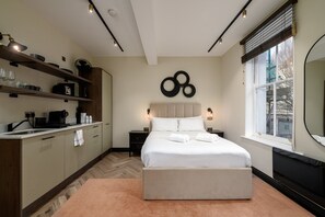 Ein modernes Schlafzimmer mit Bett, Nachttischen, einem Einbauschrank, einer Küchenzeile und einem großen Fenster.