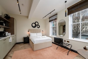 A modern bedroom with a large bed, bedside tables, a mirror, and a window with blinds. - GuestReady - Sleek studio in Euston (London)