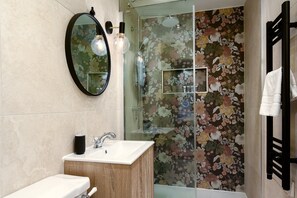 A bathroom with a round mirror, a sink, a shower with a glass door, and a towel rack. - GuestReady - Sleek studio in Euston (London)