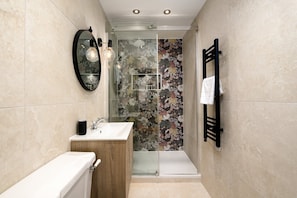 A bathroom with a toilet, sink, mirror, and shower area. - GuestReady - Sleek studio in Euston (London)