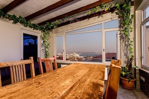 A dining area with a wooden table and chairs, large windows with a city view, and green plants. - Serene 3BR Spacious Apartment with Indoor Terrace & Bosphorus Views (istanbul)
