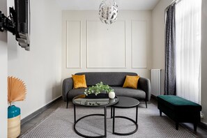En moderne stue med en grå sofa, to runde sofaborde, en grøn fodskammel og en pyntende plante.