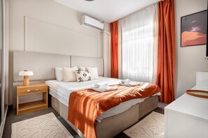 Et hotelværelse med en seng, et natbord med lampe, en hvid kommode og et vindue med gardiner.