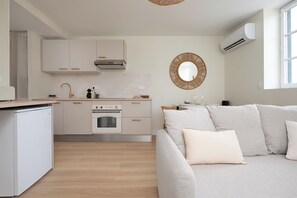 Eine moderne Küche mit weißen Schränken, einem eingebauten Backofen und einem Essbereich mit einem hellen Sofa und einem runden Spiegel an der Wand.