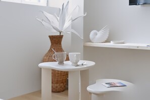 Ein weißer Tisch mit zwei Tassen und einem Löffel, eine weiße Vase mit einer Pflanze und eine Zeitschrift auf einem kleinen Beistelltisch.