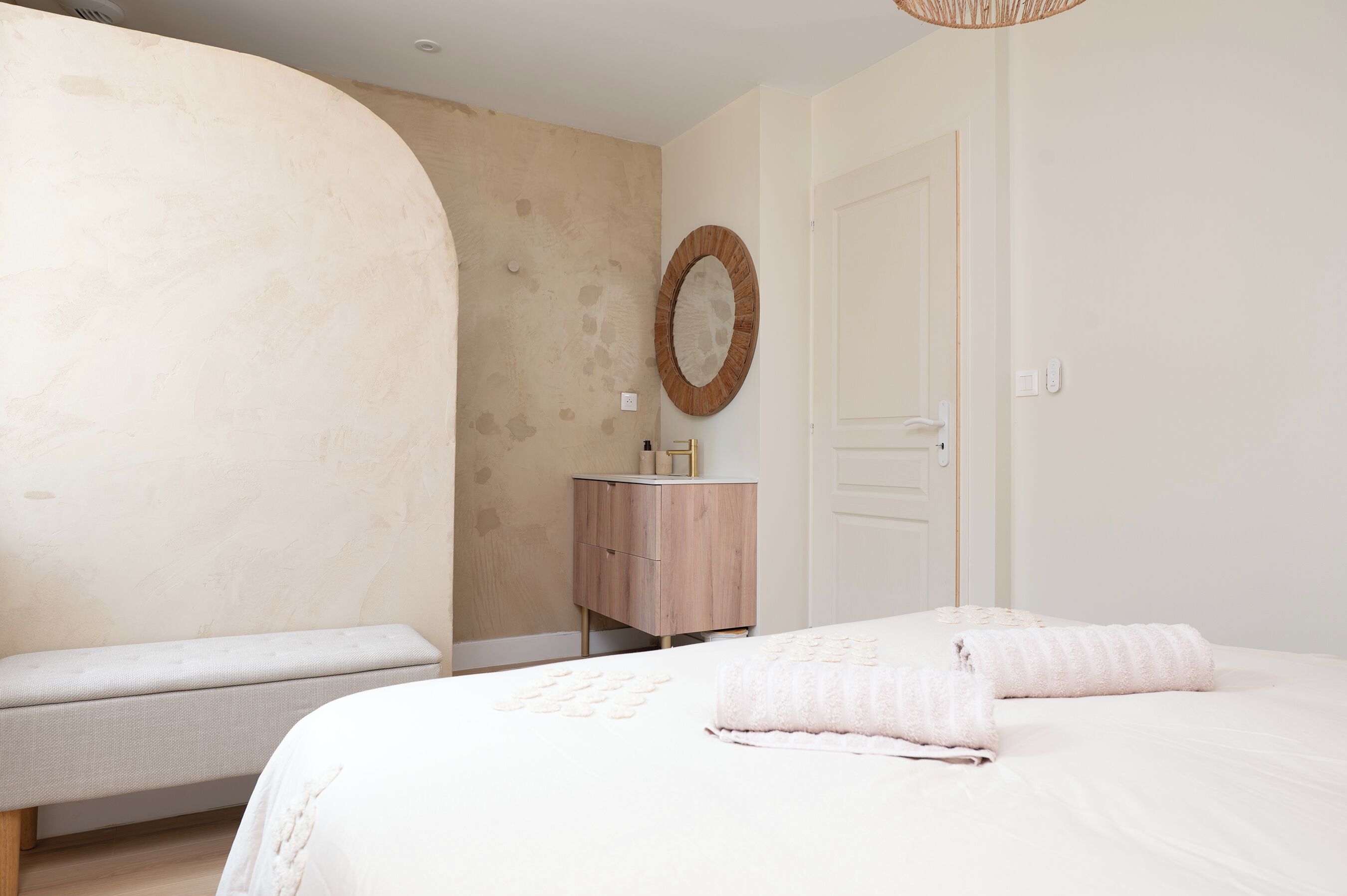 A bedroom with a bed, a bench, a wooden cabinet, and a door.
