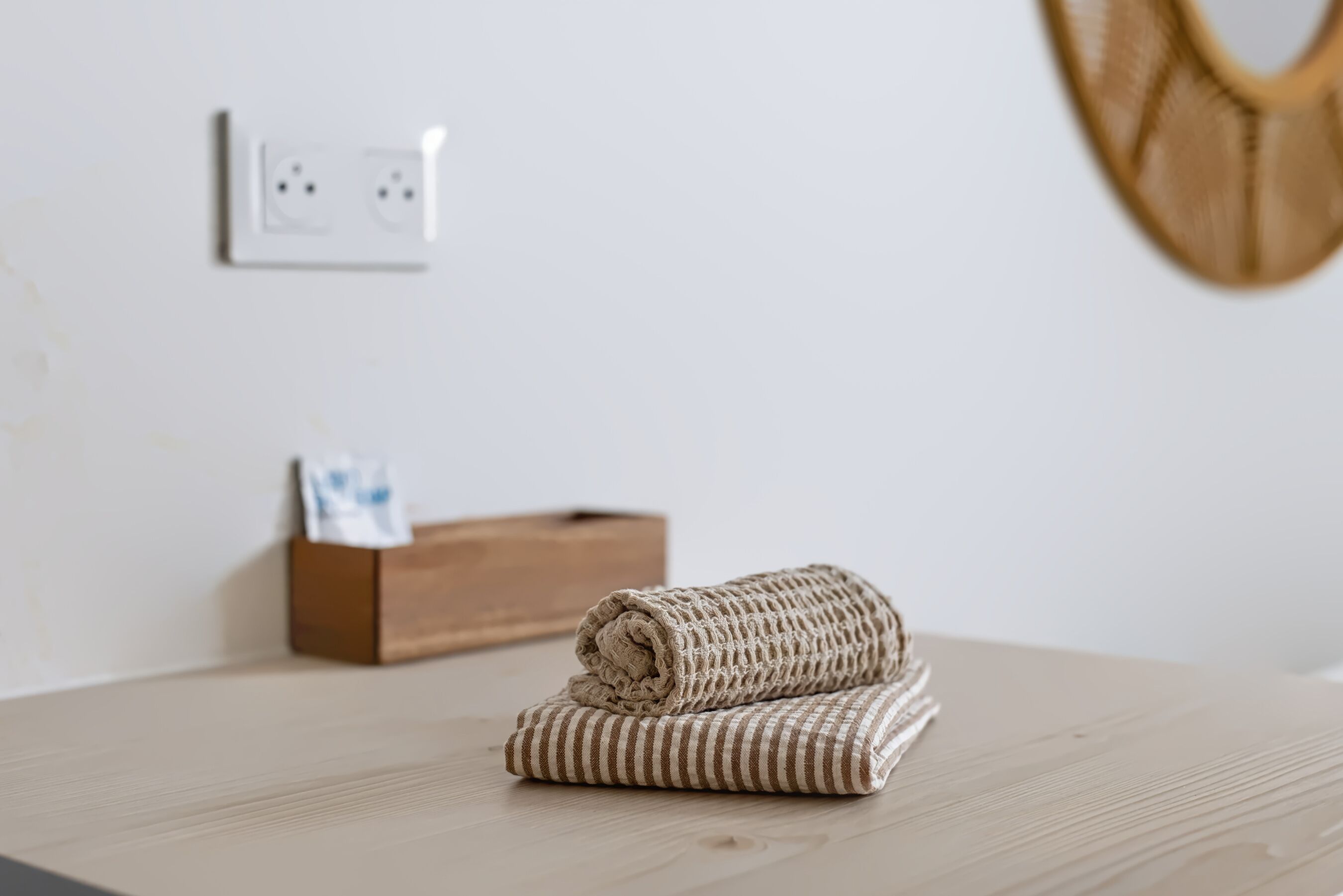 A neatly folded beige towel on a wooden table with a power outlet and a wooden box in the background.