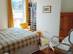 Ein Schlafzimmer mit einem Bett, einem Sessel, einem Bücherregal und einem Holzschrank.