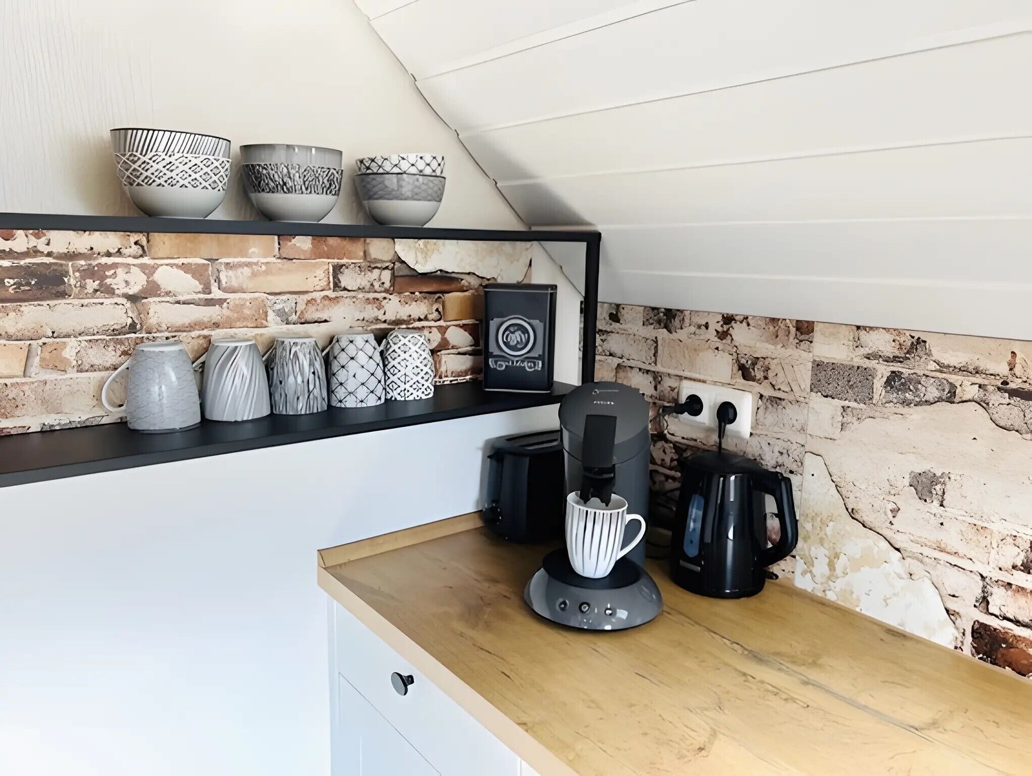 A kitchen with a brick wall, a coffee machine, and various kitchenware on a shelf.