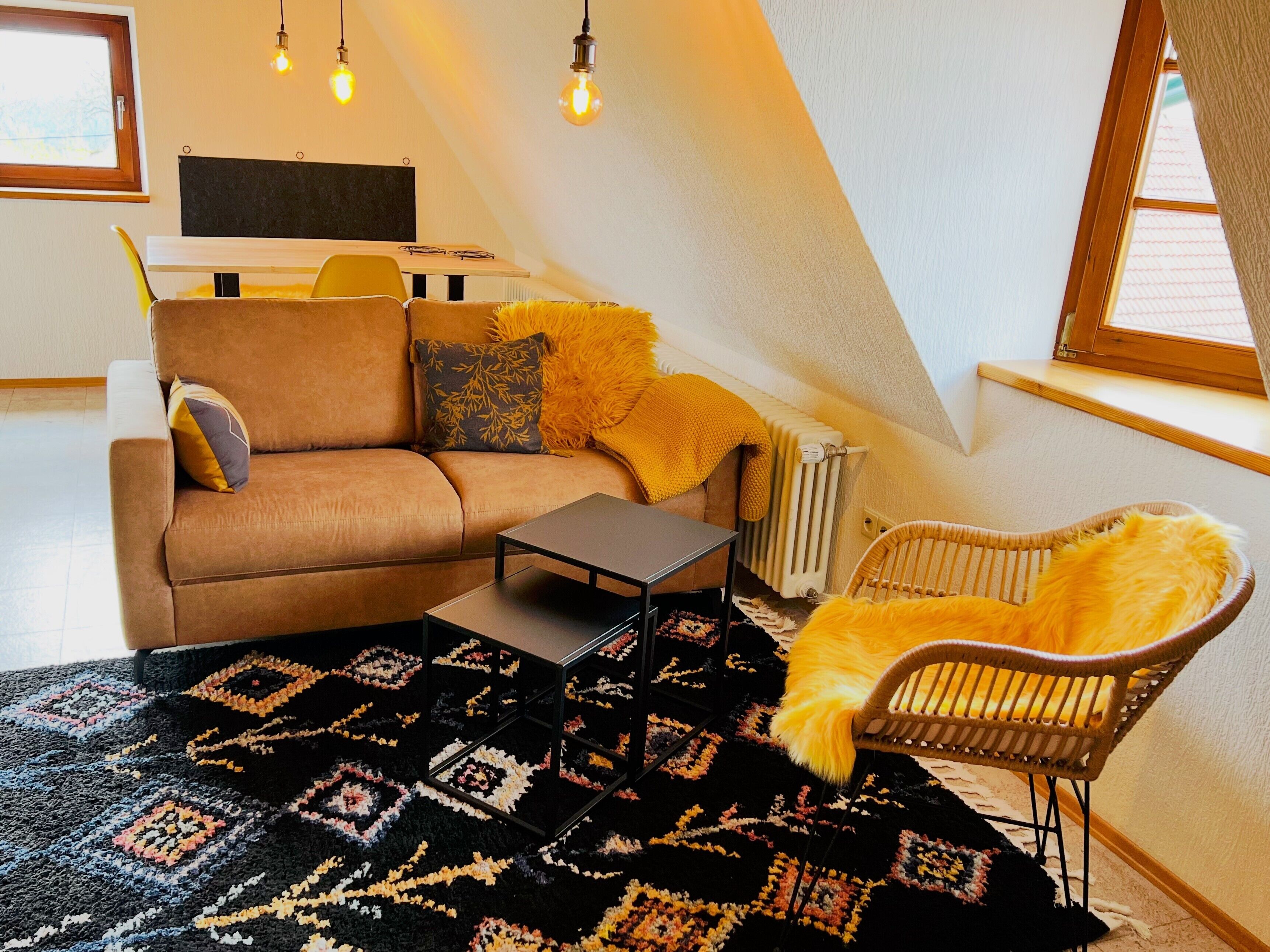A cozy living room with a sofa, a coffee table, a patterned rug, and a wicker chair.