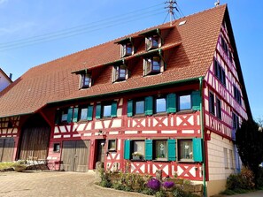 Ein traditionelles Fachwerkhäuschen mit rotem Dach, mehreren Fenstern und einer großen Holztür.