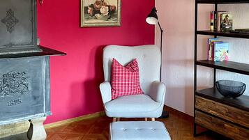 A room with a red wall, a grey armchair with a red pillow, a bookshelf, and a decorative plate with a crest.