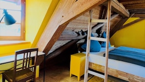 Habitació amb sostre inclinat, un llit amb roba de llit blava, una cadira de fusta i una petita taula de nit groga.