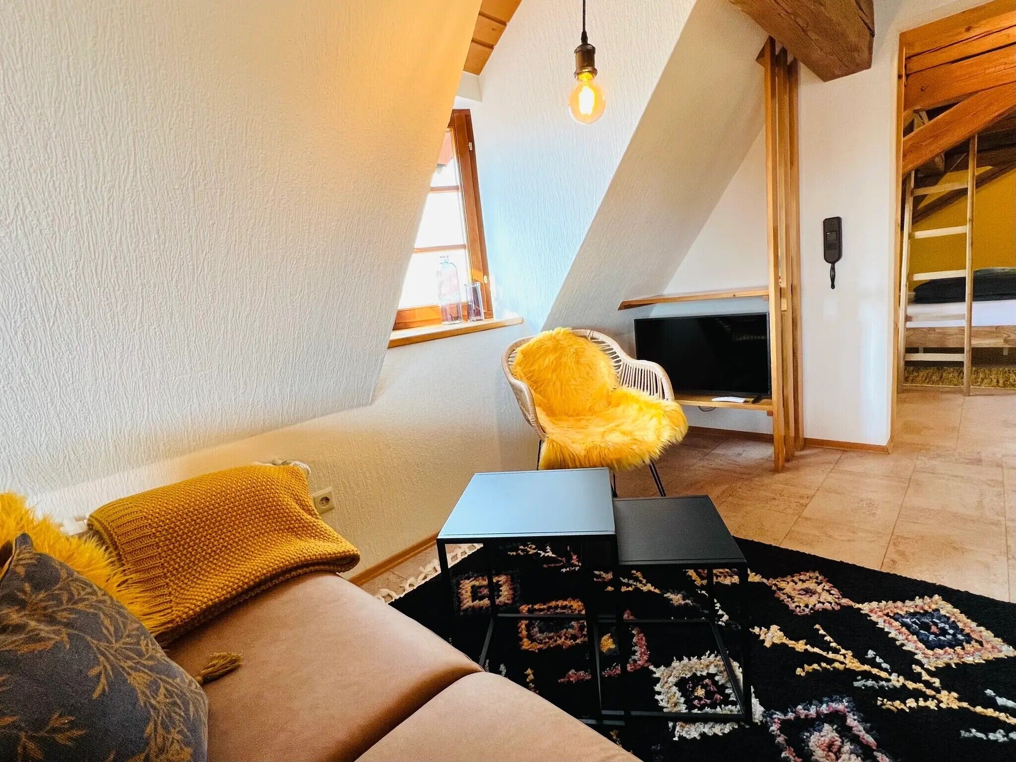 A cozy loft bedroom with a sloped ceiling, a bed with a yellow throw, a small table, and a TV.