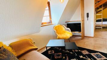 A cozy loft bedroom with a sloped ceiling, a bed with a yellow throw, a small table, and a TV.