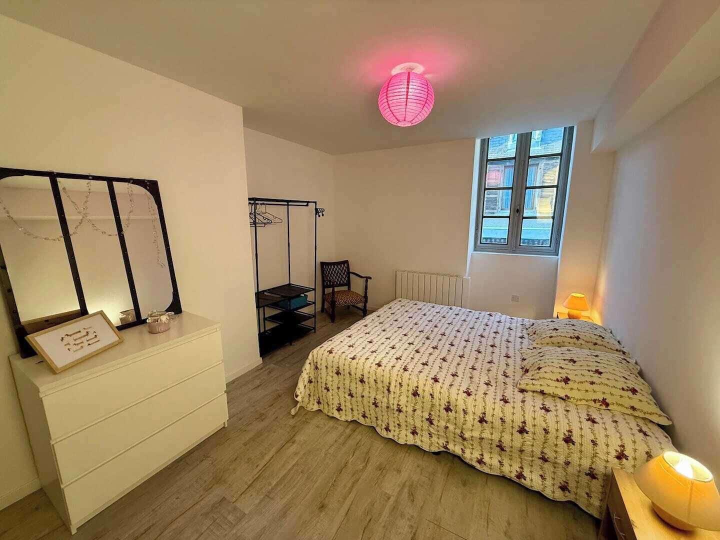 Een slaapkamer met een bed, een stoel, een dressoir, een hangstoel, een raam en een plafondlamp.