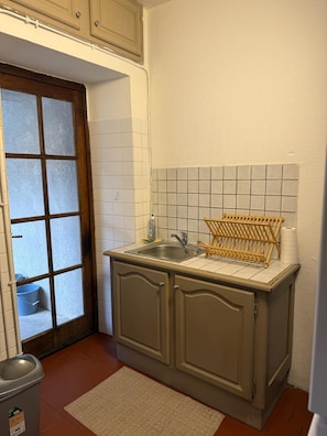 A small kitchen with a sink, a wooden drying rack, and a door leading to a storage area.