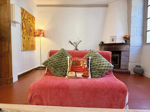 A room with a red upholstered sofa, a fireplace, and a framed picture on the wall.