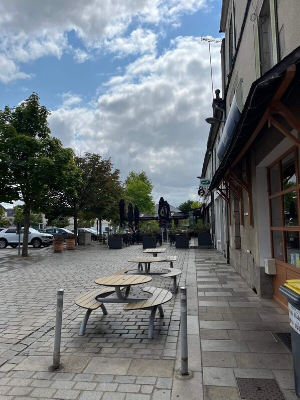 An outdoor seating area with tables and chairs, a paved walkway, and a building with a sign.