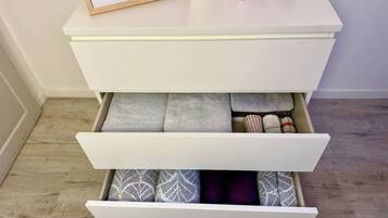 A white bedside table with a framed picture, a candle, and a drawer with patterned bedding.