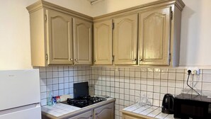 Una cocina con armarios color beige, un refrigerador blanco, una estufa, un microondas y una cafetera.
