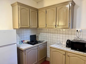 A kitchen with beige cabinets, a white refrigerator, a stove, a microwave, and a coffee maker.