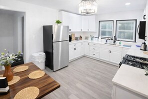 Een moderne keuken met witte kastjes, een roestvrijstalen koelkast, een eettafel met geweven placemats en een kroonluchter.