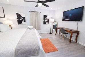 Een hotelkamer met een bed, bureau, stoel, televisie, kunstwerken en een plafondventilator.