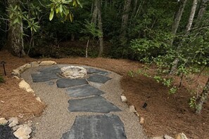 Ein Steinweg führt zu einer runden Sitzgruppe, umgeben von Tannenhäcksel und Bäumen.
