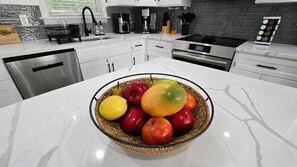 A kitchen with a stainless steel dishwasher, a coffee maker, and a fruit bowl on the counter. - BlueHaven House | Premium Executive Residence (East Haven)