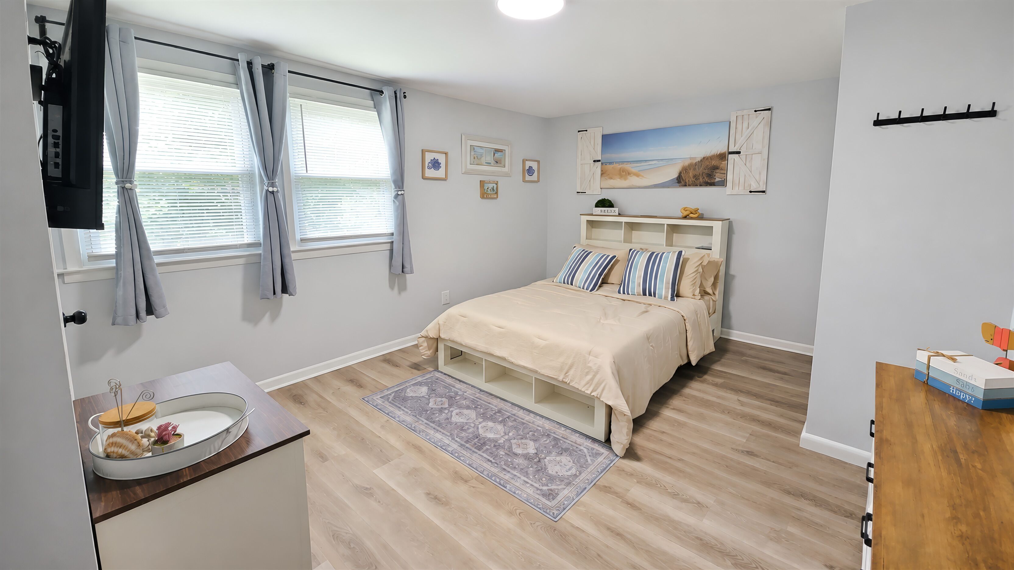 A bedroom with a bed, bedside tables, a dresser, a window with curtains, and a wall-mounted shelf with decorative items.