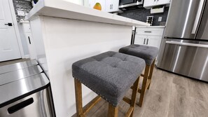 A modern kitchen with stainless steel appliances, wooden stools with grey cushions, and a white countertop. - BlueHaven House | Premium Executive Residence (East Haven)