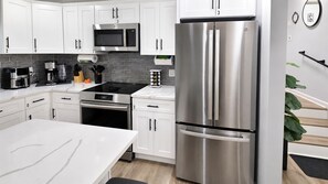 A modern kitchen with white cabinets, stainless steel appliances, and a black countertop. - BlueHaven House | Premium Executive Residence (East Haven)