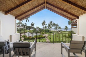 A balcony with two chairs, a view of a landscaped garden, and a beach in the background. - Flamingo Ocean front Condo (Playa Flamingo)